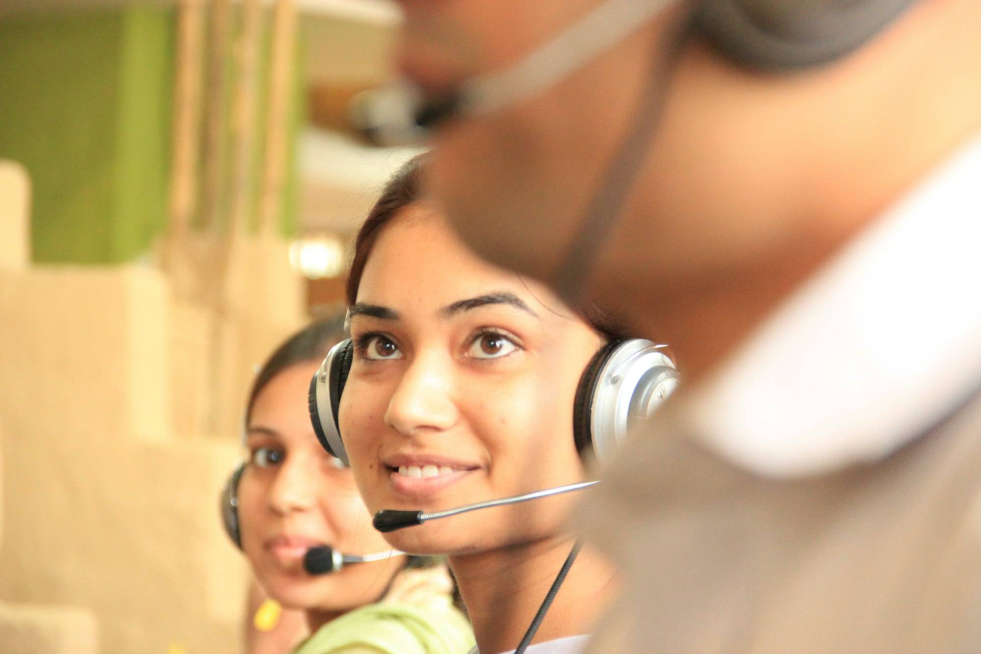 Two smiling women wearing headsets taking calls in a bright office